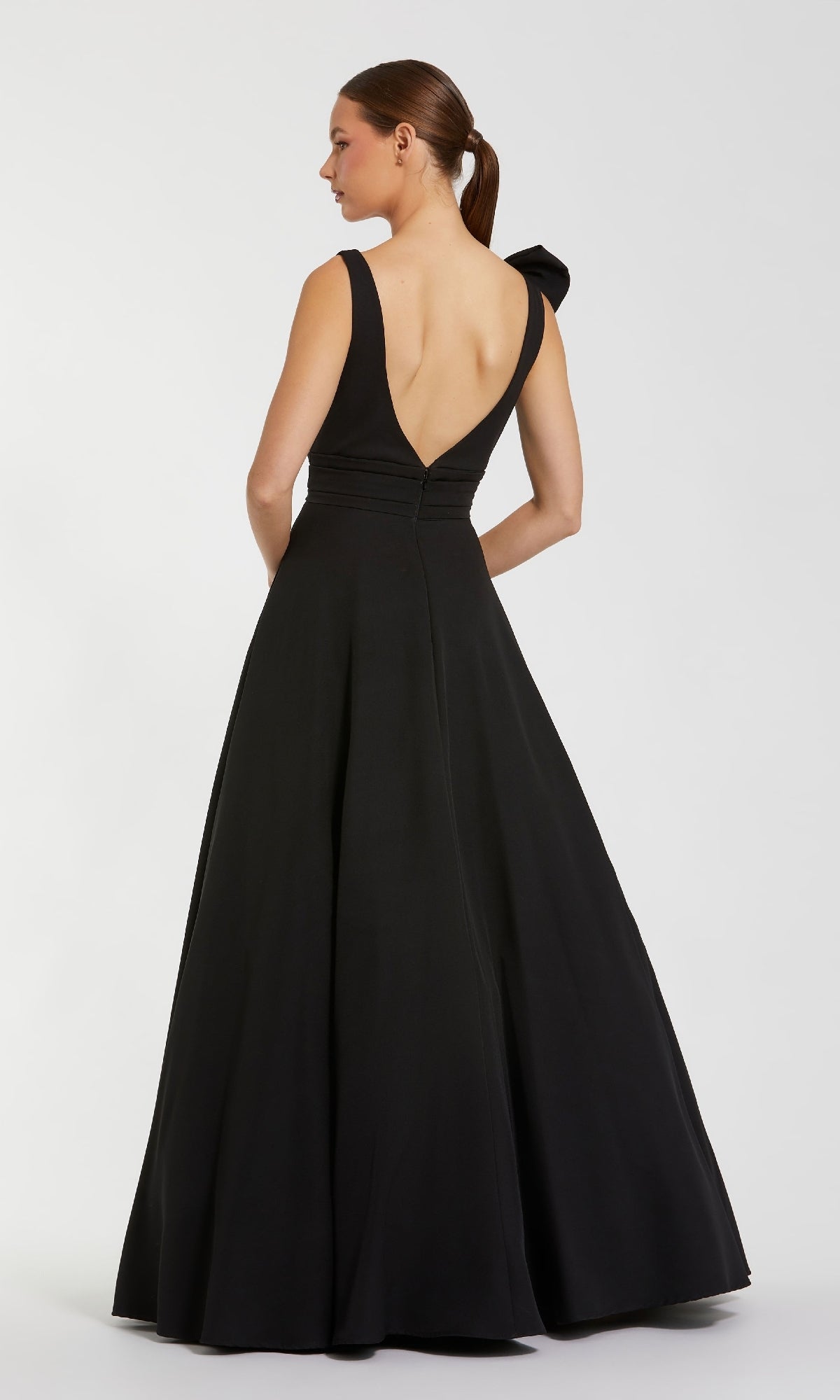A woman stands facing away from the camera in a sleeveless, floor-length Mac Duggal 49972 Shoulder-Bow Long Formal Dress with a deep V-back, set against a plain background.